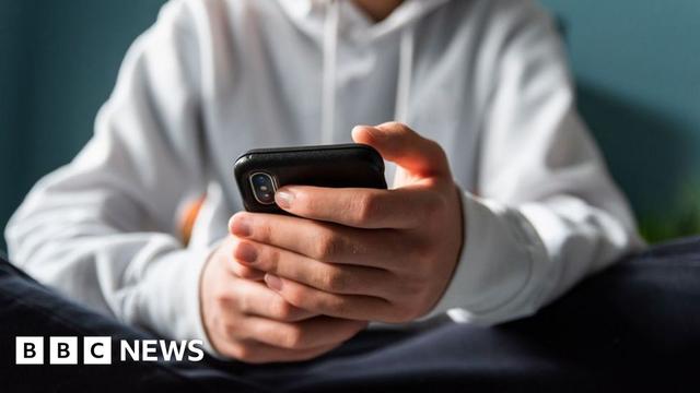 Close up of hands of teen boy in white sweater looking at a phone
