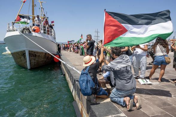 People gather with Palestinian flags around the Freedom Flotilla ship "Handala" ahead of the boat's departure for Gaza at a port in Syracuse, Sicily, southern Italy, on July 13, 2025.