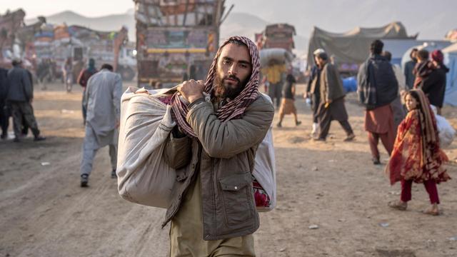 Ein geflüchteter Afghane steht in Pakistan an einem Grenzübergang. Er trägt Habseligkeiten bei sich und blickt dabei in die Kamera.