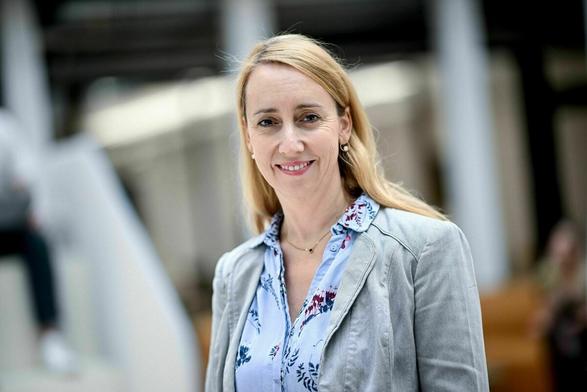 Eine blonde Frau mit bunter Bluse lächelt in die Kamera