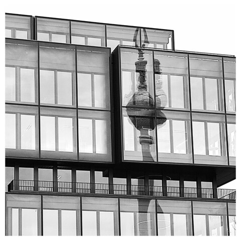 In einer Fassade mit vielen Fenstern spiegelt sich der Berliner Fernsehturm. Schwarz-Weiß-Foto