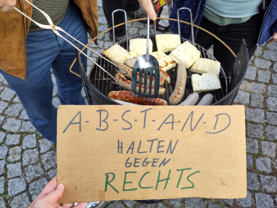Grill mit Grillgut und Schild "Abstand halten gegen Rechts"