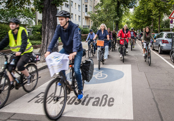 Viele Menschen fahren mit dem Rad über die neue Straße. Auf der Straße ist das große Fahrradstraßensymbol.