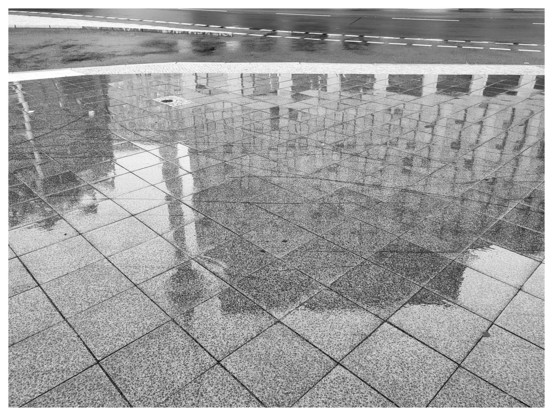 Schwarz-Weiß-Foto. Auf nassen Steinplatten spiegeln sich der Berliner Fernsehturm und zwei andere Gebäude.