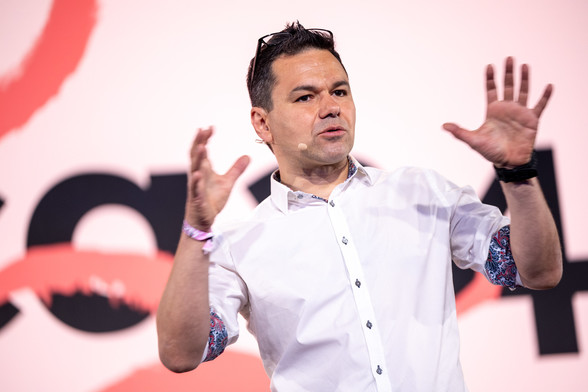 Der Sprecher Özden Terli auf der re:publica 24. Er trägt kurze schwarze Haare, ein weißes Hemd und eine Brille, die er sich auf den Kopf geschoben hat.