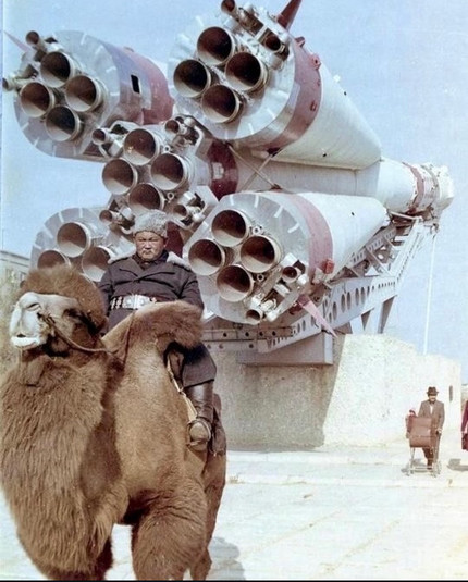 A man in military uniform astride a camel poses in front of a Soyuz rocket.