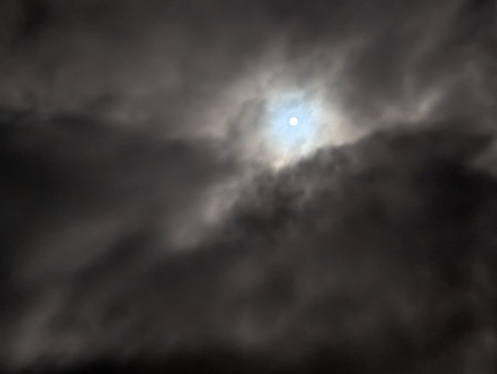 Written with the help of ChatGPT:

This image shows a close-up of the night sky. Dense, dark clouds dominate the scene, but leave an opening in their centre through which the waxing moon is visible. The moon appears as a bright point of light, its rays diffusely penetrating the clouds and gently illuminating them. The clouds appear dynamic, almost dramatic, and convey a mystical atmosphere. The combination of darkness, movement and the light of the moon creates a mysterious and slightly eerie atmosphere.