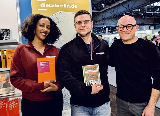 Bafta Sarbo, René Arnsburg (Manifest Verlag) und Martin Beck (Dietz Berlin) auf der Buchmesse Leipzig: Bafta hält Walter Rodneys »Dekolonialer Marxismus« in Händen, René dessen Standardwerk »Wie Europa Afrika unterentwickelte«.