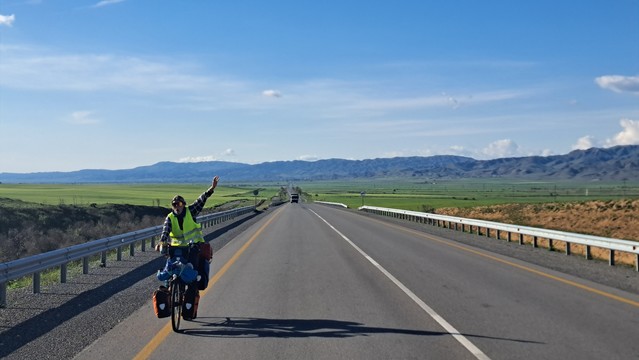 Fahrradfahrerin mit erhobener Hand vor weiter Landschaft 