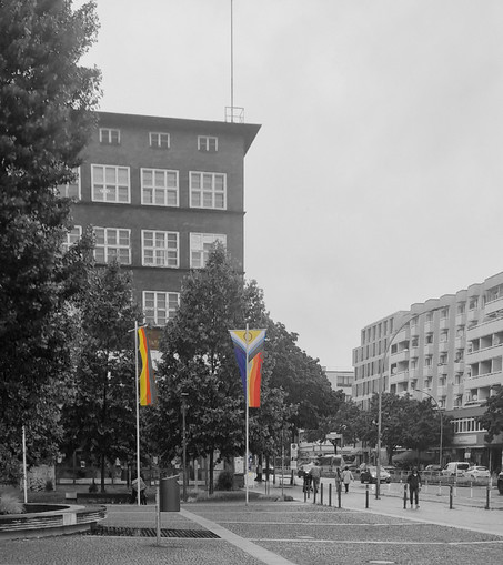 Zwei Regenbogenflaggen wehen vor dem Rathaus Wedding. Im Hintergrund ein Backsteingebäude und moderne Wohnhäuser.

