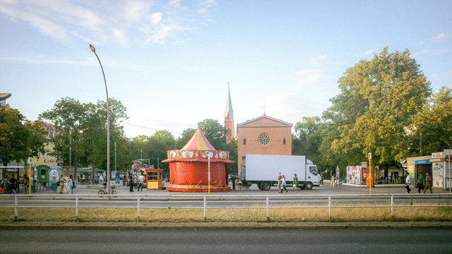 Roter Kinderkarussell-Aufbau mit Transporter auf dem Leopoldplatz, im Hintergrund die Nazarethkirche und umliegende Geschäfte.

