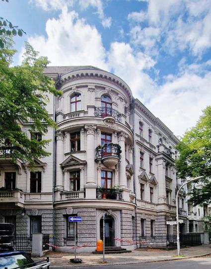 Historisches Wohngebäude im Stil der Gründerzeit mit runder Eckfassade, verzierten Balkonen und großen Fenstern an einer Straßenecke in Berlin-Wedding.

