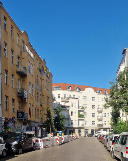 Straßenszene in Berlin-Wedding mit Altbauten, geparkten Autos und Baustellenabsperrungen bei sonnigem Wetter.

