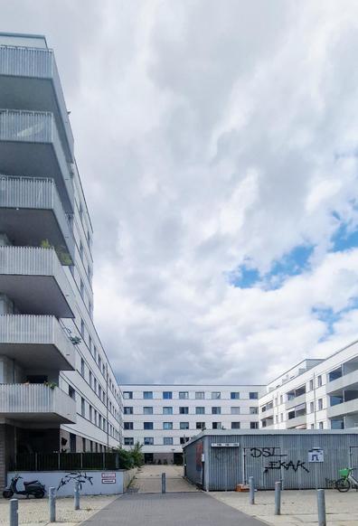Alt-Text: Neubau-Wohnanlage in Berlin-Wedding mit weißen Fassaden, Balkonen und einem Innenhof, vorne ein Container mit Graffiti.

