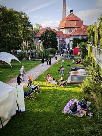 Grünfläche vor der Alten Heiz-Kraftzentrale in Berlin-Wedding mit Menschen auf Liegestühlen und Picknickdecken beim Pop-Kultur Festival.

