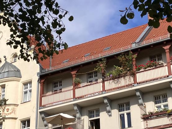 Historische Hausfassade mit roten Balkongeländern, Blumenschmuck und rotem Ziegeldach.