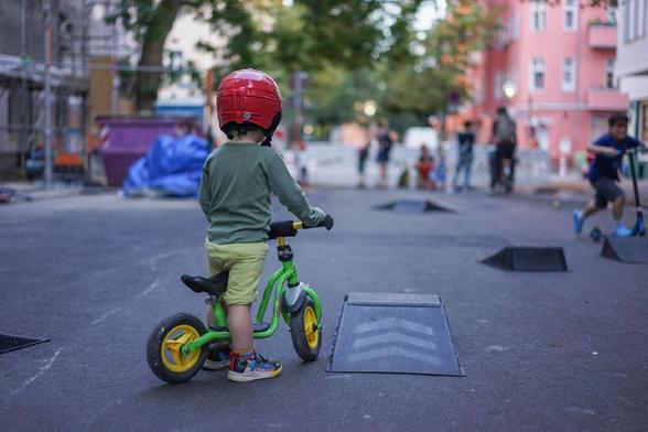 Kinder spielen auf einer für den Verkehr gesperrten Straße im Berliner Stadtteil Wedding bei einer Aktion der temporären Spielstraße; zu sehen sind unter anderem Tischtennis, Laufräder, Straßenmalkreide, Roller und ein großes buntes Schwungtuch.