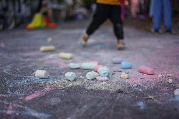 Kinder spielen auf einer für den Verkehr gesperrten Straße im Berliner Stadtteil Wedding bei einer Aktion der temporären Spielstraße; zu sehen sind unter anderem Tischtennis, Laufräder, Straßenmalkreide, Roller und ein großes buntes Schwungtuch.
