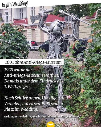 Alt-Text: Metallskulptur eines Menschen mit erhobener Axt vor dem Anti-Kriegs-Museum im Berliner Stadtteil Wedding, umgeben von Rosensträuchern.

