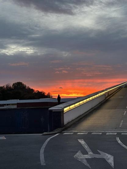 Blick auf eine Brücke im Berliner Stadtteil Wedding bei Sonnenuntergang, mit einer Person am Geländer und einem leuchtend orange-roten Himmel im Hintergrund.