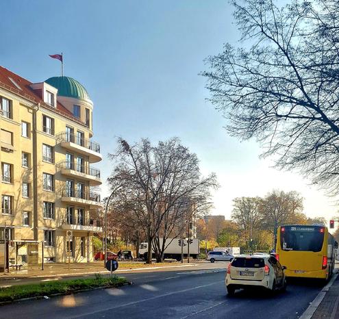 Straßenszene in Berlin-Wedding mit einem gelben BVG-Bus der Linie 221 und einem Taxi an einer Ampel. Links steht ein mehrstöckiges Wohnhaus mit grünem Kuppeldach und wehender Fahne, im Hintergrund sind kahle Bäume und parkende Fahrzeuge zu sehen.