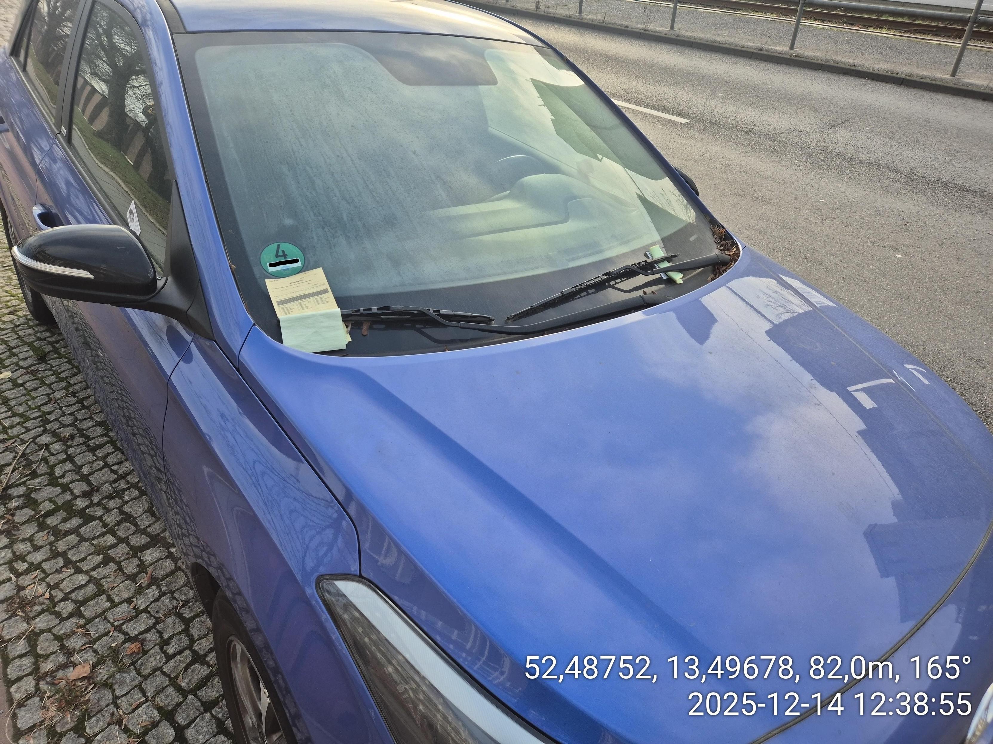 ein blauer PKW mit drei Zetteln unter dem linken Scheibenwischer, einem unter dem rechten Scheibenwischer