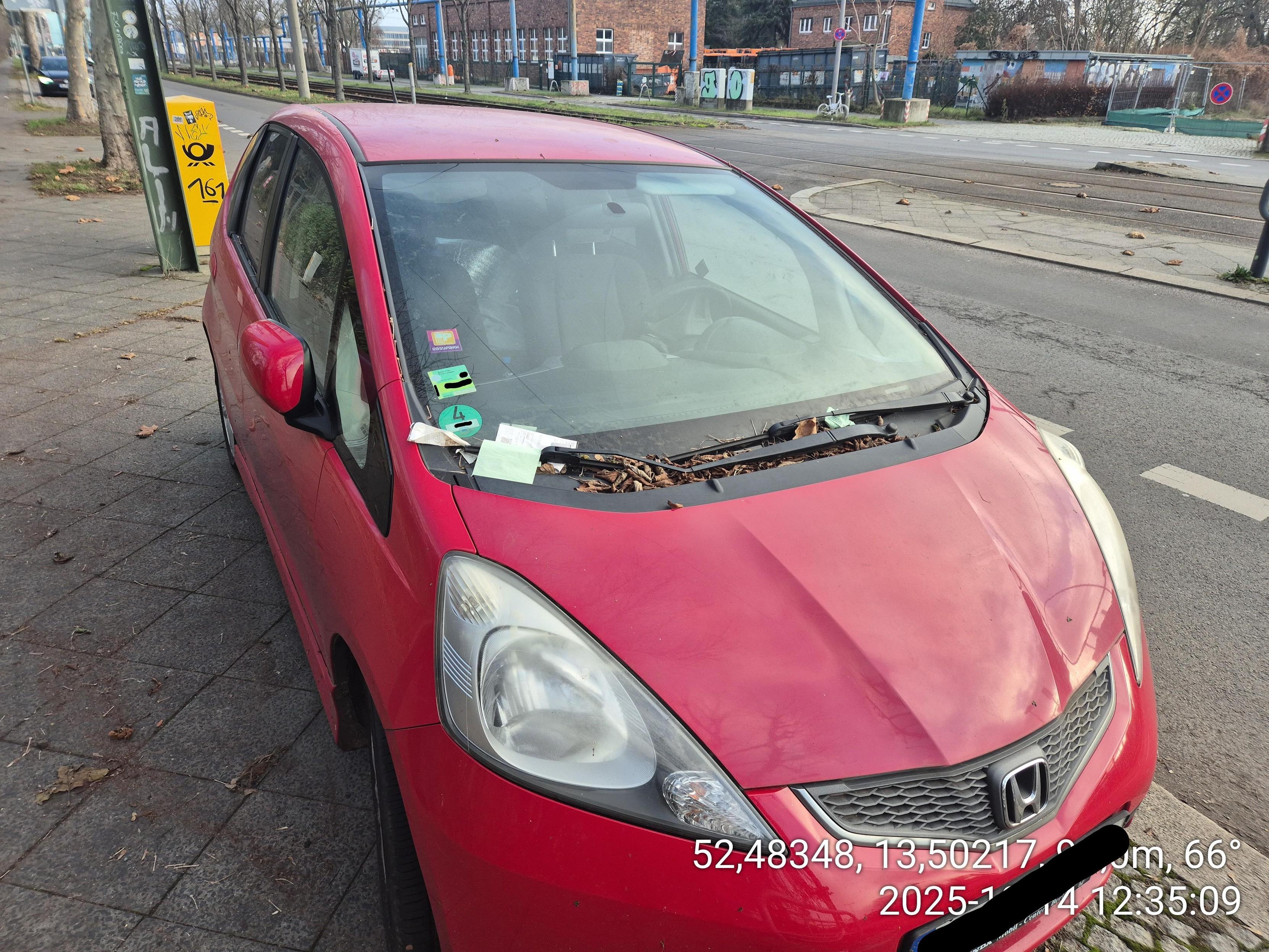 ein roter PKW mit 4 Zetteln unter dem linken Scheibenwischer, einem unter dem rechten Scheibenwischer