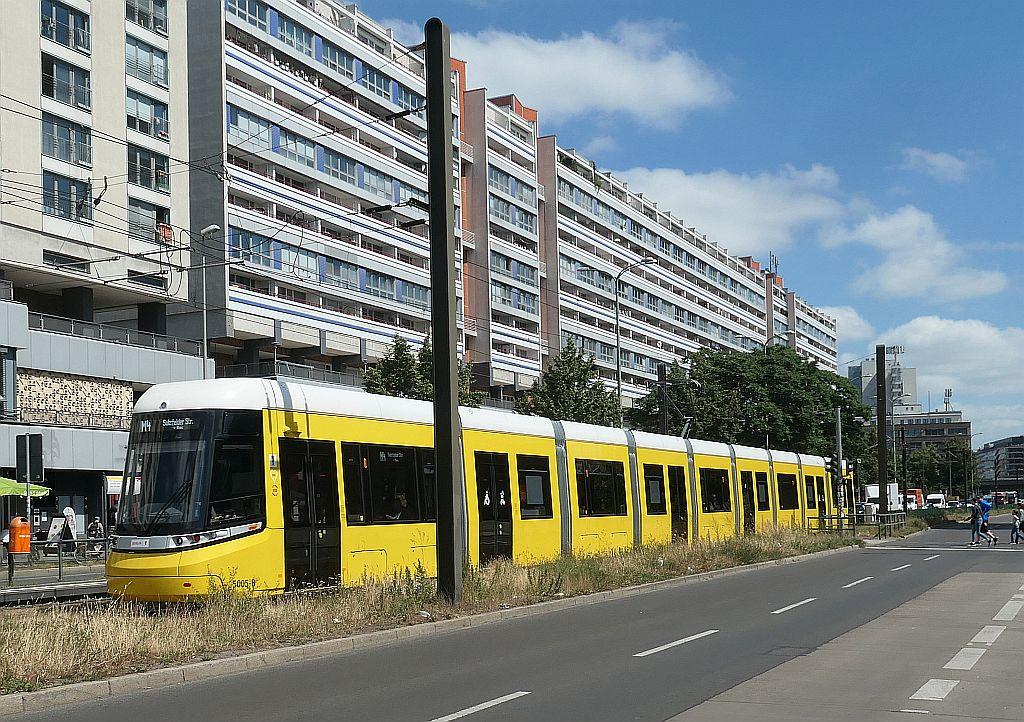 Straßenbahn im Mittelstreifen einer großen Straße mit Häusern im Hintergrund